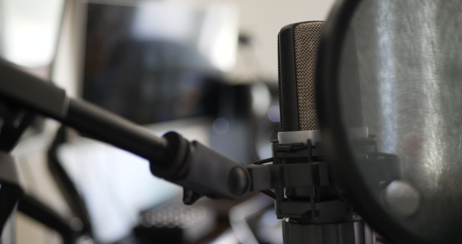 A music producer adjusting a professional condenser microphone in a music studio for recording a singer or vocalist SLIDE LEFT.