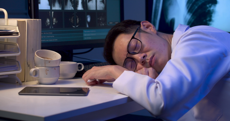Exhausted overload asian male doctor is falling asleep on desk with monitors showing x-ray film. Sleepy tired alone physician man dozing off while holding stylus in one hand at late night. Dolly shot. Royalty-Free Stock Footage #1060235312