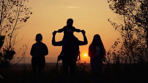 Tourists teamwork. Happy family in the park. Hiker hiking climbing. Happy family of tourists with backpacks going hiking. Silhouette group of tourists in the park at sunset.Teamwork on Hiking.
