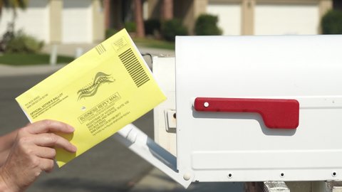 Close up of a woman's hand returning mail ballot, putting into post box. Illustrative editorial taken in Vista, CA / USA on October 7, 2020.