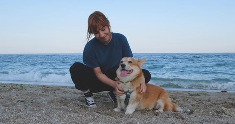 Young woman play with corgi dog on the sea beach
