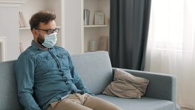 Isolated Sick young caucasian Young man in medical protective mask sitting on a sofa, coughing, sneezing at home. coronavirus, quarantine, pandemic time - Powered by Shutterstock - Get 15% off with code: PIKWIZARD15