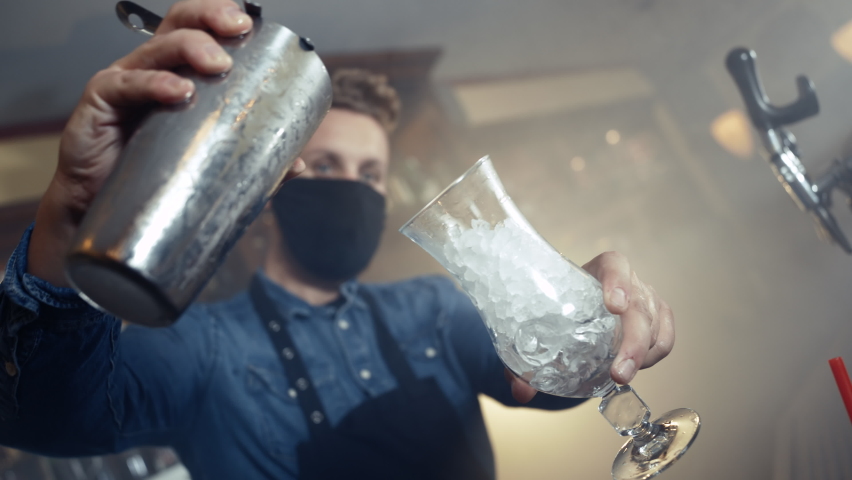 Barkeeper wearing face mask and an apron spilling cocktail in glass in smoky bar shot in 4k super slow motion | Shutterstock HD Video #1060241900