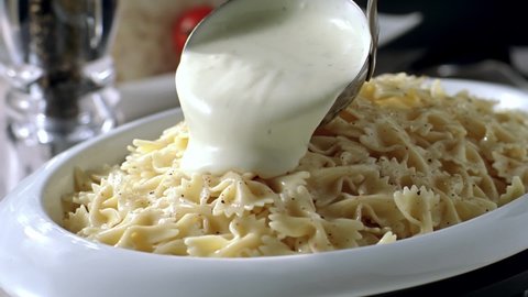 The sauce is poured over the pasta on the serving plate in slow motion. Yogurt sauce pouring into the pasta.