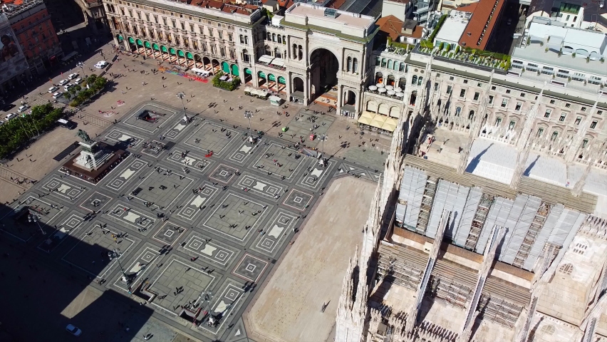 Aerial view of Piazza Duomo in front of the gothic cathedral in the center. Drone view of the gallery and rooftops during the day. Flight over the city. People in the city. Milan. Italy,