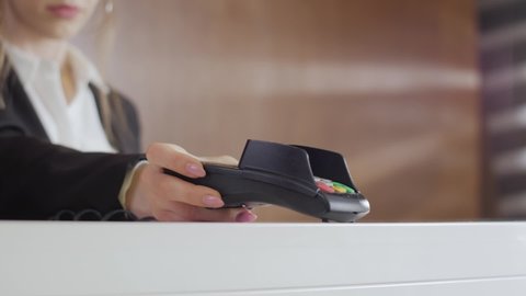 Close up hand making payment with credit card machine terminal while swiping debit card or credit card to pay the bill. Woman hand enters the credit card pin to make the payment through terminal pos.