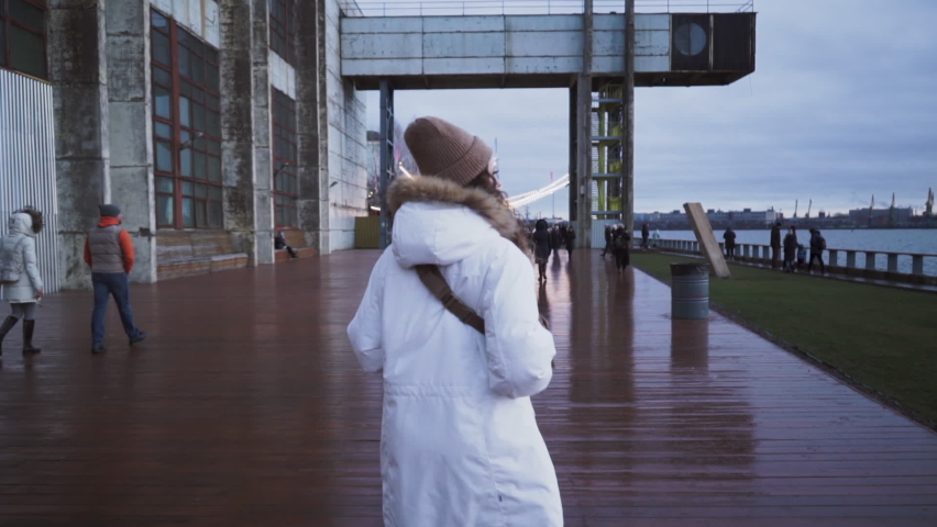 Norwegian girl walks down the street. Scandinavian Foggy seascape. Young woman in a white jacket. Cloudy overcast dramatic landscape. Blue time