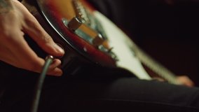 Closeup man hand sticking plug to guitar in concert hall. Unrecognizable person connecting instrument in recording studio. Unknown sound engineer preparing electric guitar for playing. - Powered by Shutterstock - Get 15% off with code: PIKWIZARD15