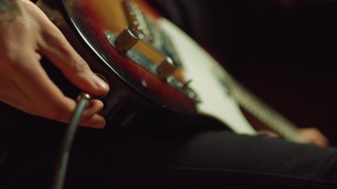 Closeup man hand sticking plug to guitar in concert hall. Unrecognizable person connecting instrument in recording studio. Unknown sound engineer preparing electric guitar for playing.