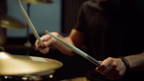 Unrecognizable musician hands hitting drum plates in recording studio. Close up of drummer hands performing solo with drumsticks. Attractive artist playing on drum kit indoor.