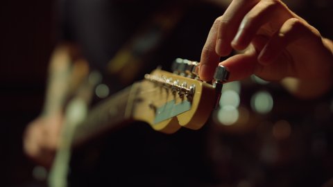 Unrecognizable man tuning acoustic guitar in music studio. Macro musician hand turning knobs on fretboard in concert hall. Unknown guitarist holding instrument in recording studio.