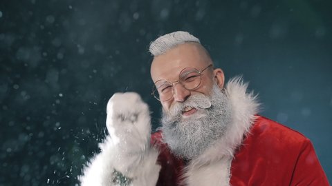 Portrait of Funny Kind Santa Claus Blows Snow Looking at Camera, Waves Hand Closeup Indoor. Magical Greeting Gesture for Winter Holidays Spirit, Congratulation Happy New Year, Merry Christmas Surprise
