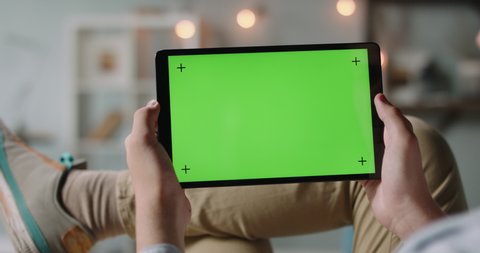 Close up shot of guy lying on couch, having an online video conference, holding tablet computer with mockup chroma key green screen and talking 4k footage
