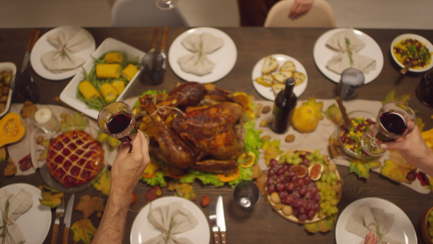 Top view shot footage of unrecognizable people clinking glasses with wine above dining table full of delicious food for Thanksgiving celebration
