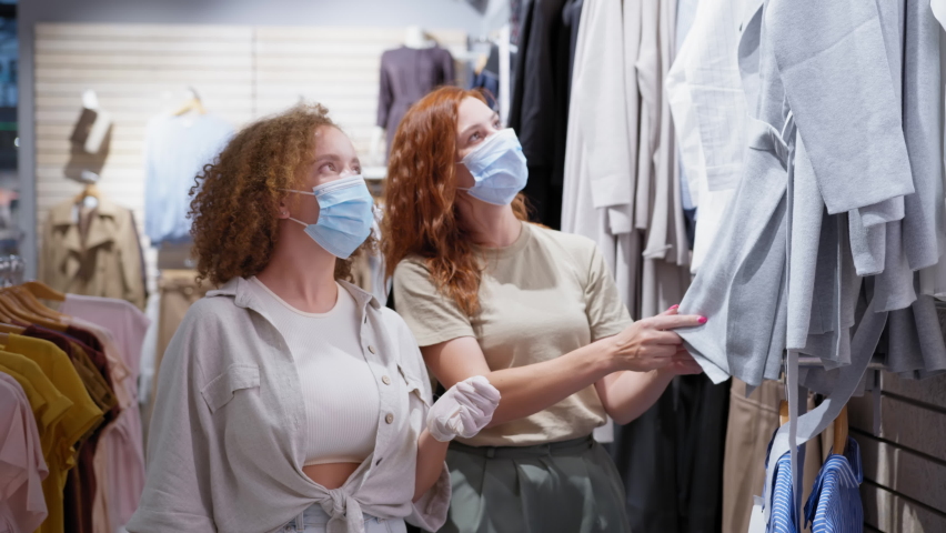 Shopping in store, charming female customers wearing medical masks choosing clothes from new collection in shop after quarantine was lifted, small business | Shutterstock HD Video #1060262480