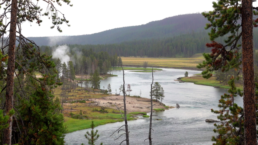 Landscape in Yellowstone National Park with Yellowstone River, mountains and geothermal feature.