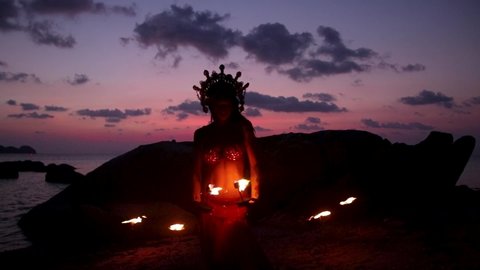Erotic and sensual belly dancer, performing spinninges with fire palm torch props, on the beach during golden hour. Slow motion.