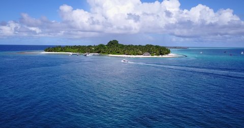 Boat approaching to small harbor of tropical island in Maldives with piers and docks close to white sandy beach, resorts and restaurants into palm trees forest