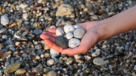 Blurry defocus Beautiful round gray, white sea stones lie in a female hand against background of beach, coast with sea stones, sea waves and foam. Concept of relaxation, meditation. Slow motion video.