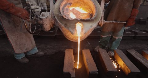 Close-up cropped view of factory workers pouring molten metal into casts at a steel casting foundry