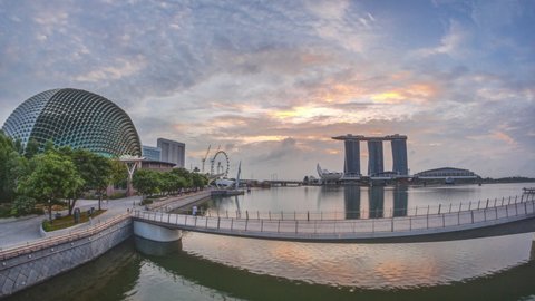 Skyline in Marina Bay with Esplanade Theaters on the Bay and Esplanade footbridge early morning timelapse in Singapore during sunrise. Skyscrapers reflected in water