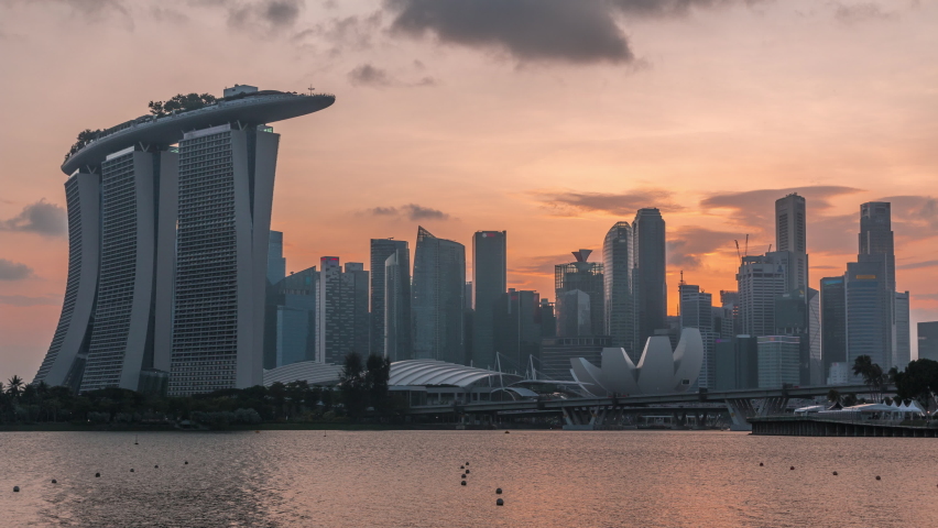 Downtown skyline of Singapore as viewed from across the water from The Garden East day to night transition timelapse. Singapore. Reflection in water with illuminated skyscrapers