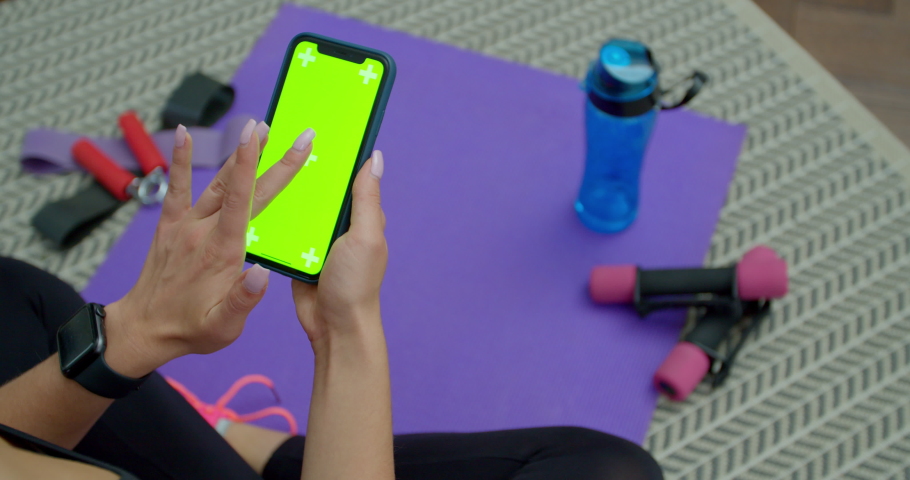 Lviv, Ukraine - October 5, 2020: Fitness woman use smartphone with green screen after training at home. Healthy lifestyle. stretching, leaning forward. Training on distance.