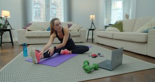 Fit and healthy woman in sportswear doing exercises with help of her instructor online on laptop at home. Training, workout and wellness concept.