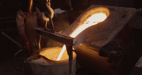 Close-up view of a factory worker pouring molten metal out a smelting furnace at a steel casting foundry