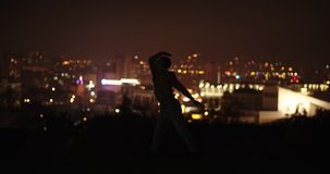 Silhouette of a male dancer dancing in the night up in the hill in front of the city lights, low key footage
