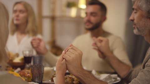 Group of four people spending Thanksgiving day together holding hands and praying to Lord in silence Video stock