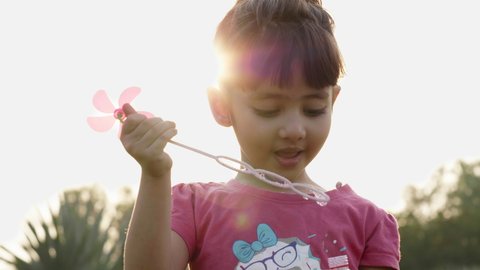 A close-up shot of a cute and adorable little girl child is blowing soap water bubbles against the sun in the park or garden. 