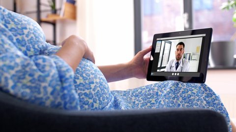 pregnancy, technology and medicine concept. happy pregnant woman with tablet pc computer having a video call with a doctor at home.
