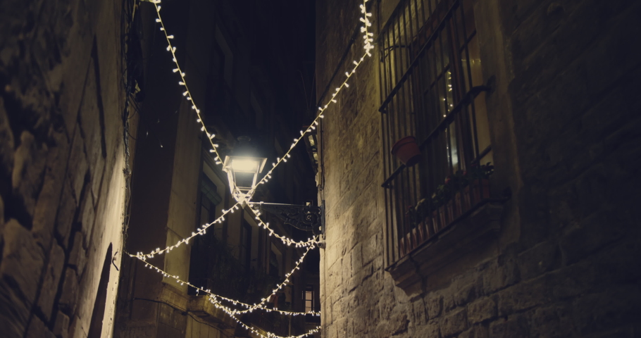 Christmas holidays lights decoration along narrow street at the night in the center of Barcelona.Night view of empty old streets of Gotico quarter with christmas lights illumination. Lamps against the | Shutterstock HD Video #1060280102