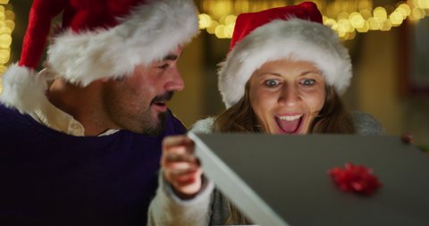 Authentic shot of happy man is making christmas gift to his beloved woman. The woman is surprised and excited after opening received gift box. Concept of holidays, romance, surprise, e-commerce