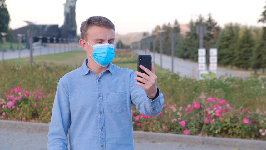 A young guy in a protective mask communicates in video chat on the street