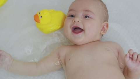 An adorable baby girl taking a bath with a duck. Closeup.