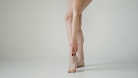 A slender young woman touches her legs with hand. Bared female legs on a white background