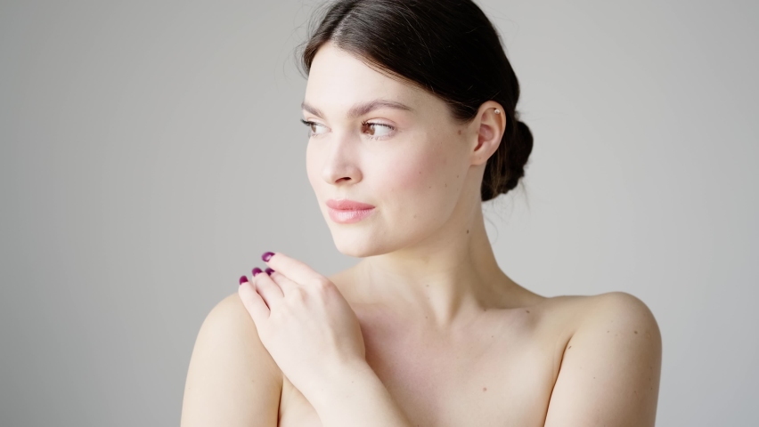 Woman close-up portrait on a white background. A young tender woman touches her bare shoulders and smiles