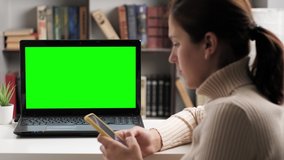 Woman is sitting at table and looking at green screen laptop, she types in on-screen keyboard and talking on internet online video connection. Chroma key computer screen woman talking on video call