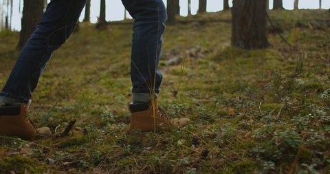 Person is walking in a forest. Close up focus on boot or hiking shoes. Close up view of man legs walking in the summer forest. Man hiking on a forest trail.