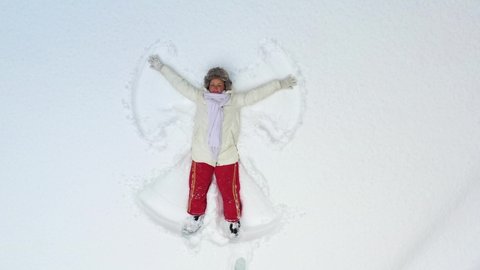 AERIAL. A young girl lying in the snow and painting an angel. The camera mowing around and zooming to the girl lying in the snow. 