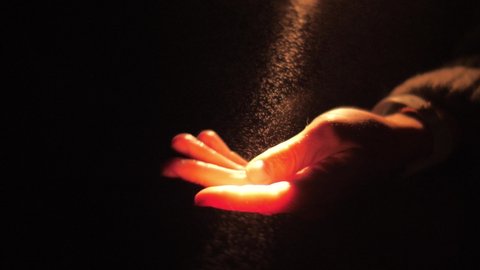 Human hand touching light particles in dark background. Fog mist shine in ray of light. God faith prayer meditation darkness night concept. Slow motion, 4K UHD