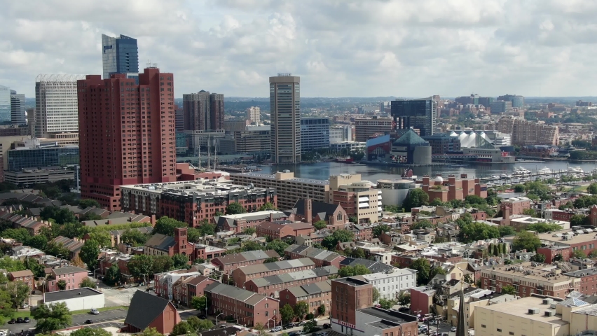 Rising aerial establishing shot as clipper ship sailboat enters Inner Harbor in Baltimore Maryland USA on summer day, city urban skyline under beautiful clouds, neighborhood ocmmunity houses below