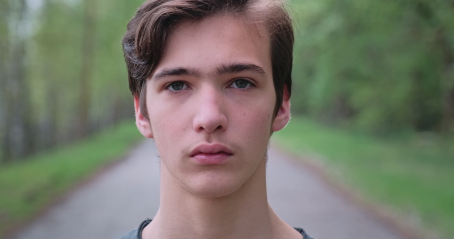 Young sad man looks on the camera. Unhappy alone young teenager, outdoors. Closeup face of  handsome guy with sad eyes, on the nature.  Closeup  frustrated teenager face, outside | Shutterstock HD Video #1060299299