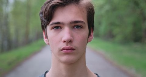 Young sad man looks on the camera. Unhappy alone young teenager, outdoors. Closeup face of  handsome guy with sad eyes, on the nature.  Closeup  frustrated teenager face, outside
