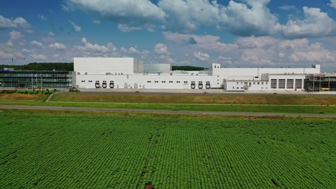 Modern industrial building. Exterior of white manufacturing on green field. Front view of a large factory. Aerial view. Camera moves forward.