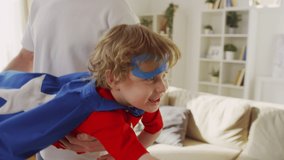 Medium shot of little pretty boy in superhero costume and blue eye mask imitating flying with fist forward while father holding him in arms horizontally - Powered by Shutterstock - Get 15% off with code: PIKWIZARD15