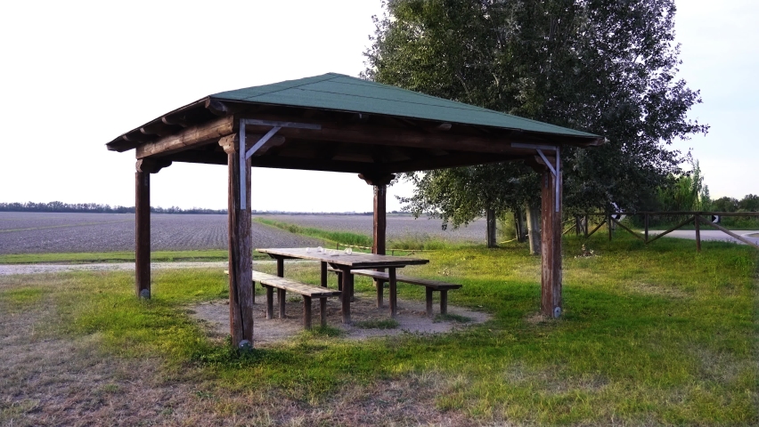 Wooden benches surround table in pavilion with green roof