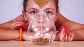 Girl with pink hair looks at sand inside sandglass at table - Powered by Shutterstock - Get 15% off with code: PIKWIZARD15